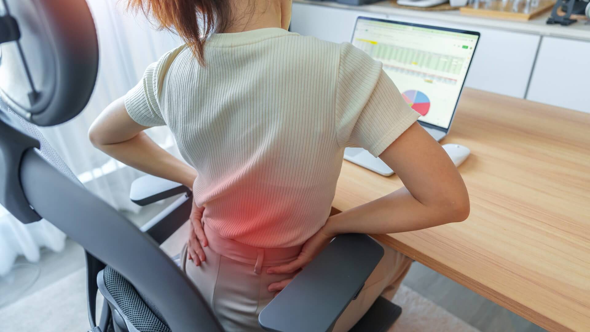 A woman sitting at her desk and stretching her sore back