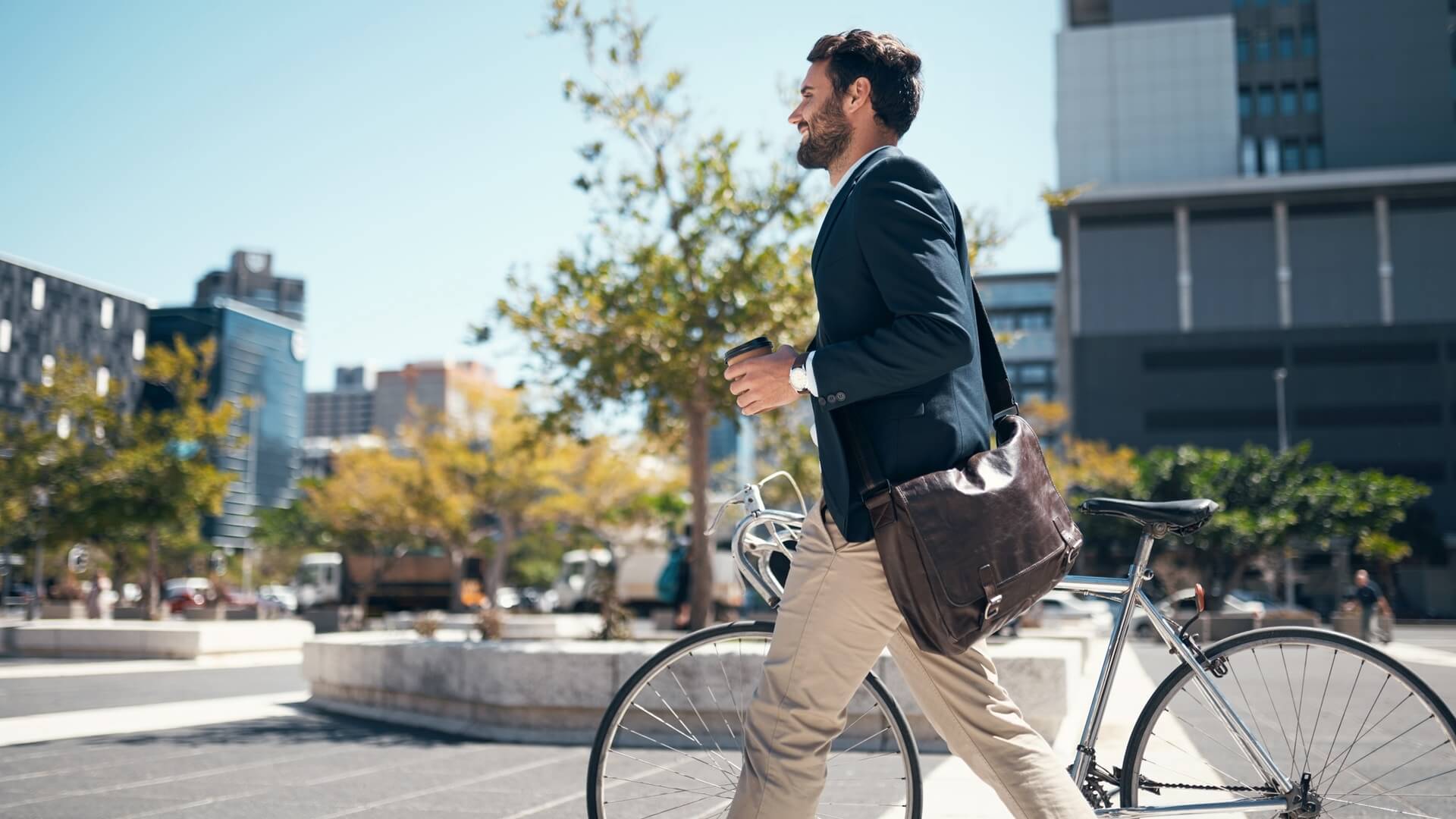 A man holding a coffee and walking his bike into work