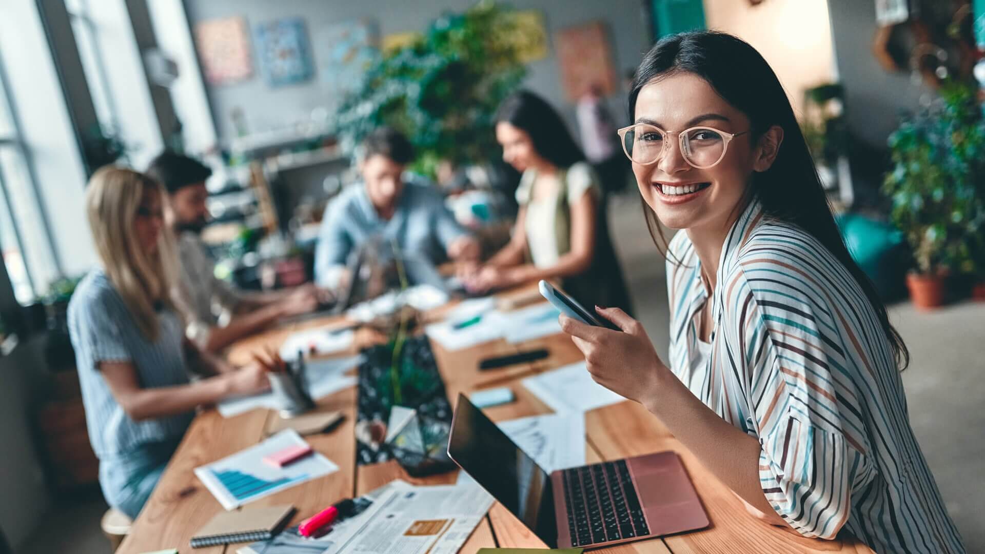 Smiling girl sitting in front pf laptop in an open plan workspace