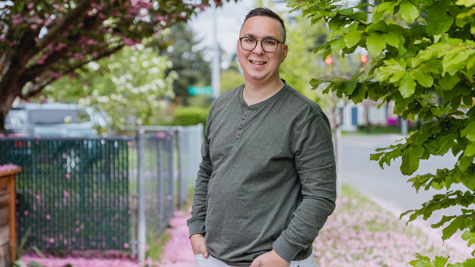 A man with autism smiles standing outside on a leafy footpath