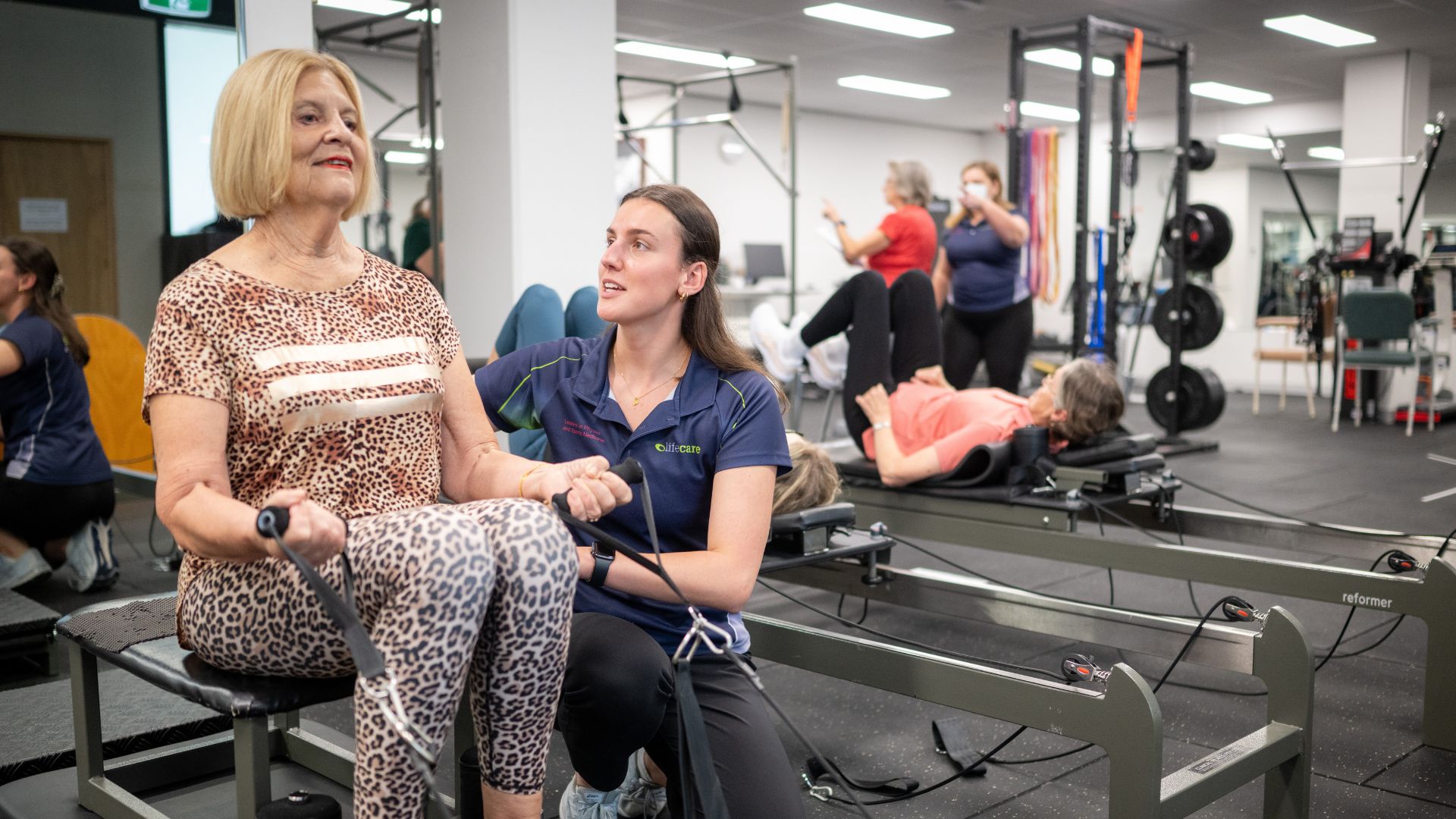 A Lifecare Croydon clinician supports a client during a reformer pilates session in the clinic gym, with other participants exercising nearby.