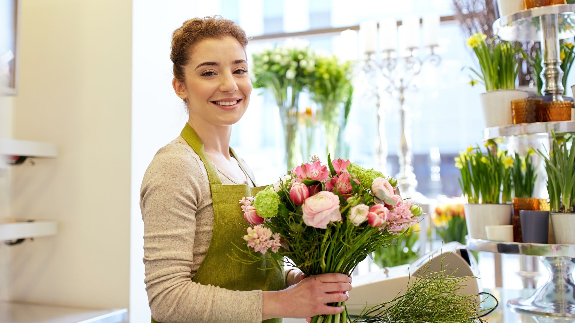 A woman smiles holding flowers in a shop