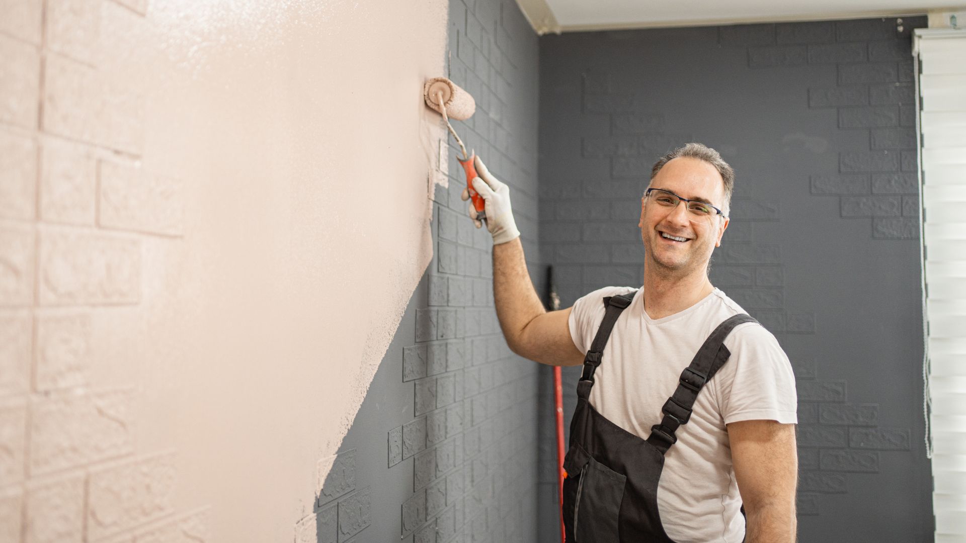 A man smiles as he paints a wall