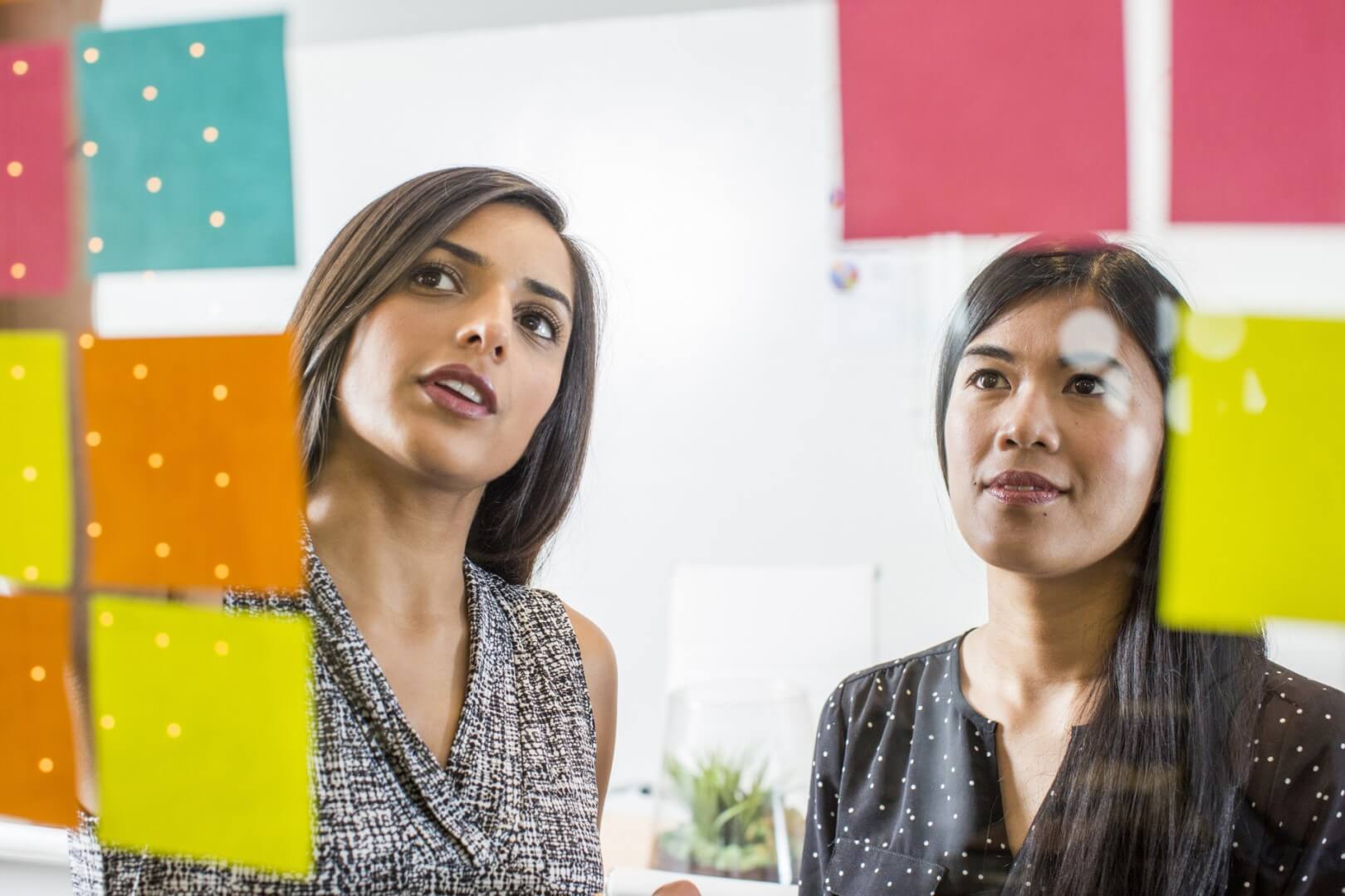 two women in the workplace having a meeting in from of a series of sticky notes