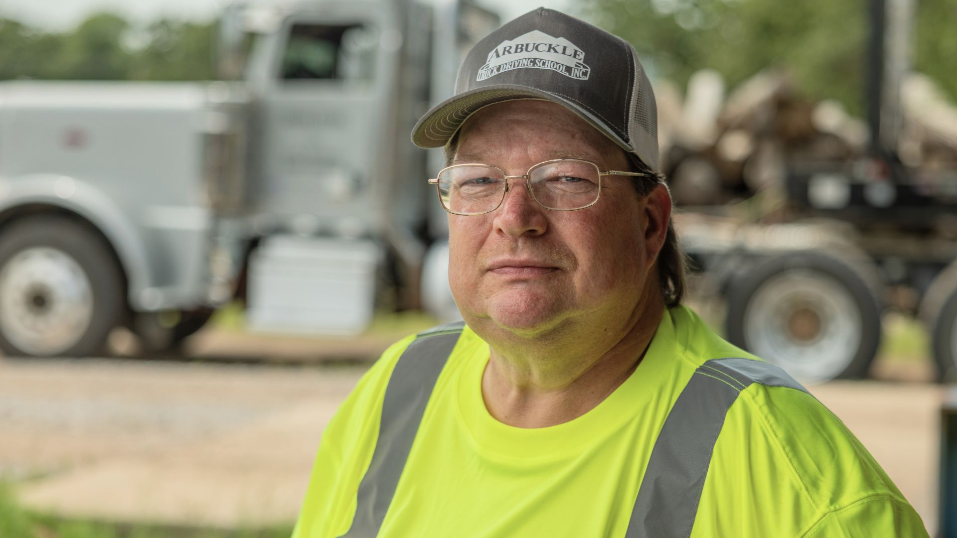 Ocie in a high-visibility vest and a cap labelled "Arbuckle" seated in front of a truck.