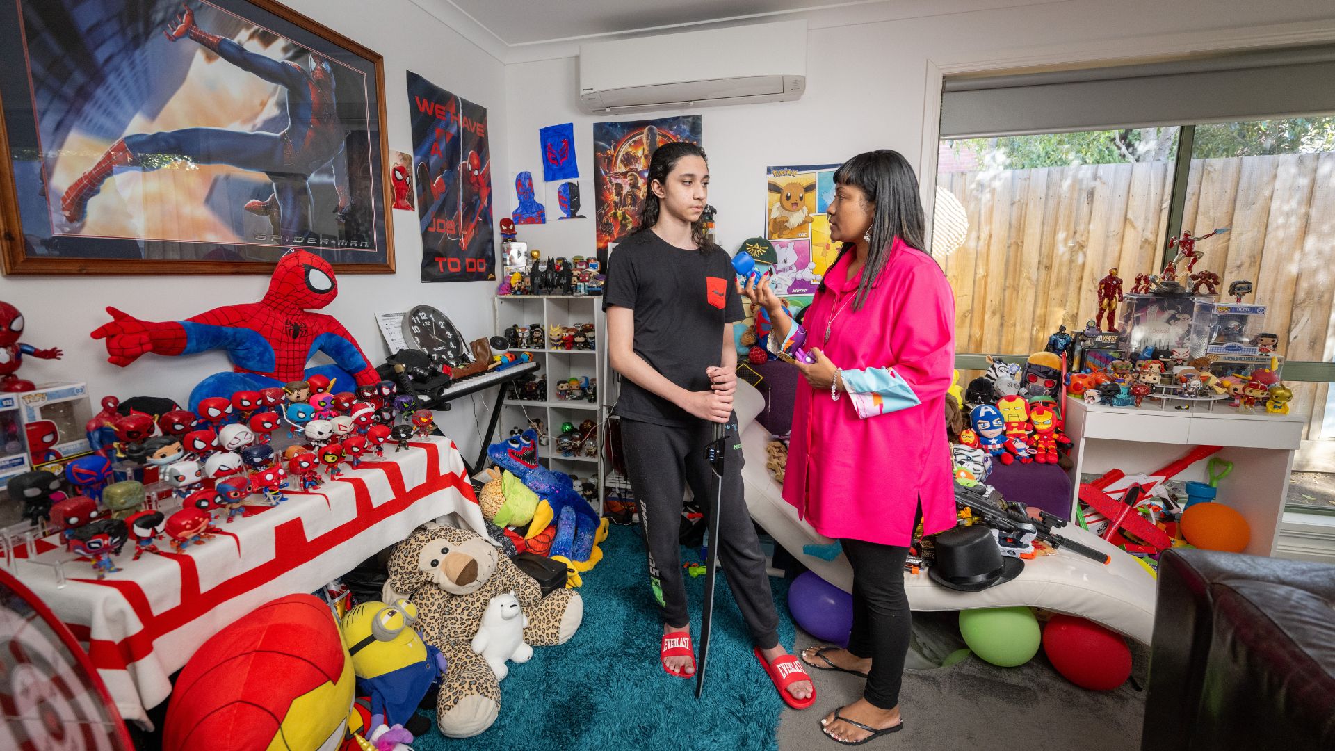 Wari talking to Conrad in a colorful room filled with superhero collectibles and toys, showing family support enabled by MyIntegra.