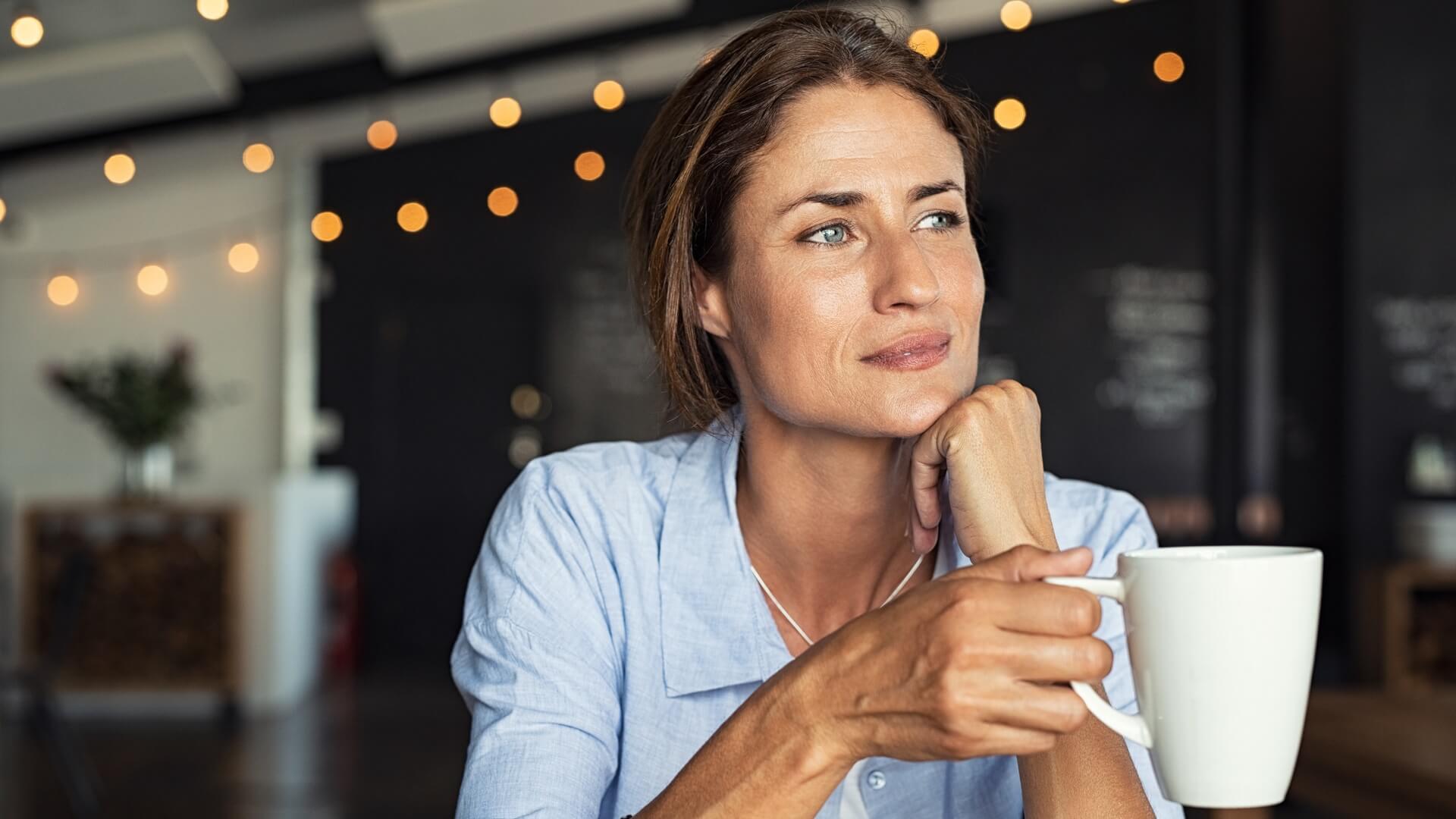 A smiling woman drinking a cup of coffee in a café