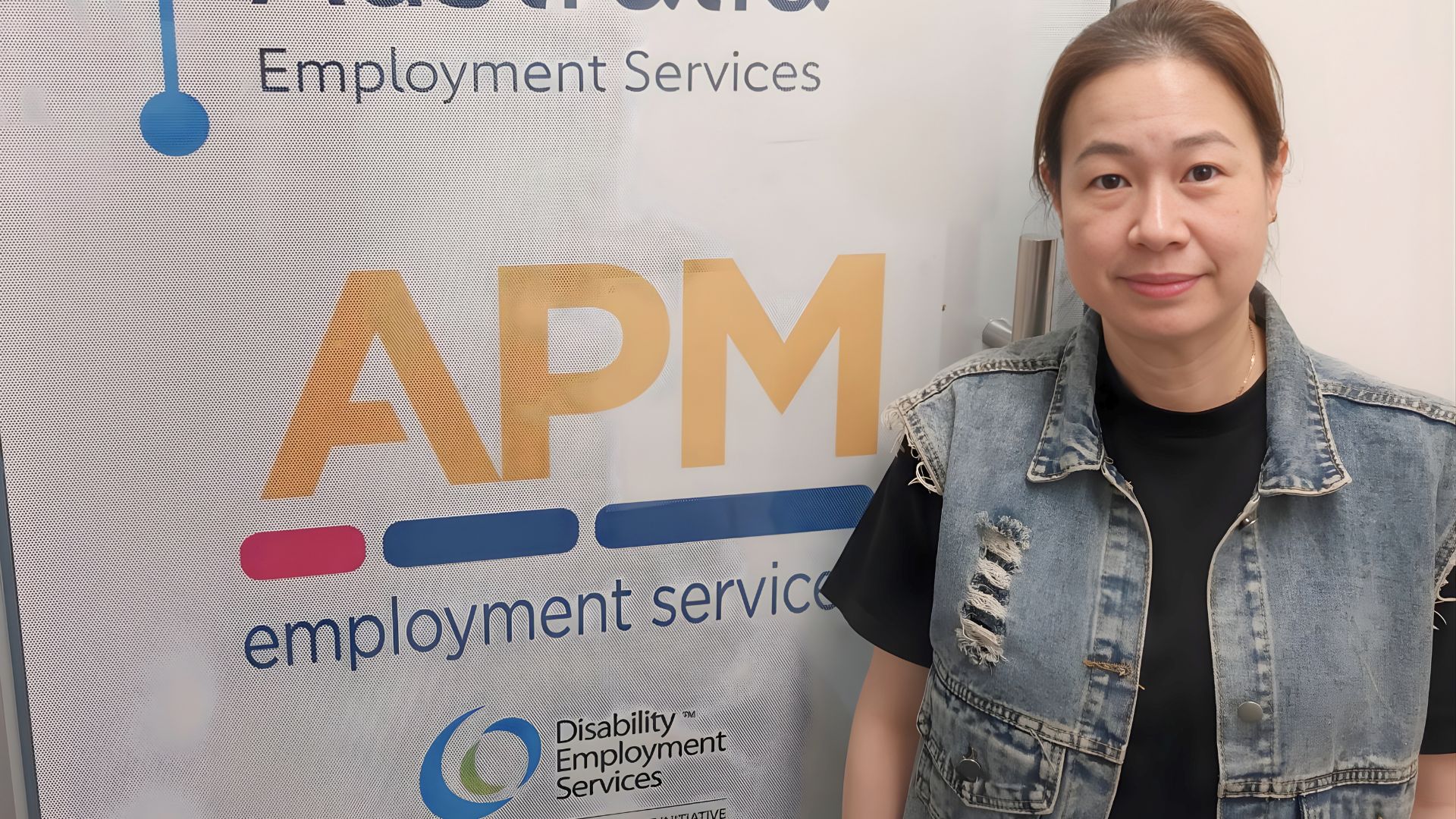 Workforce Australia participant Wicole standing in front of an APM Employment Services banne