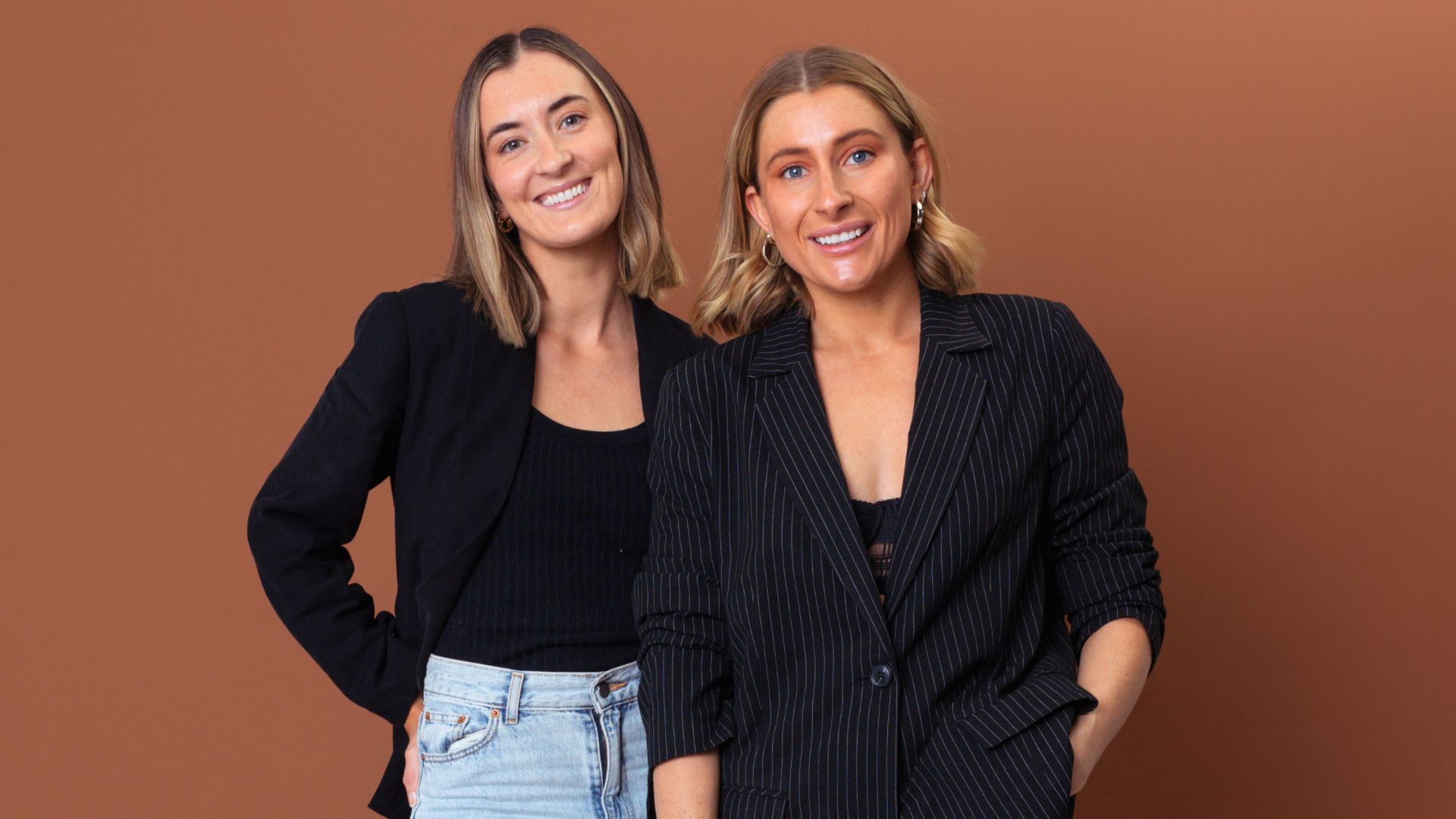 Self Employment Assistance participants Kate and Nicolette posing together in a professional studio setting against a plain brown background.