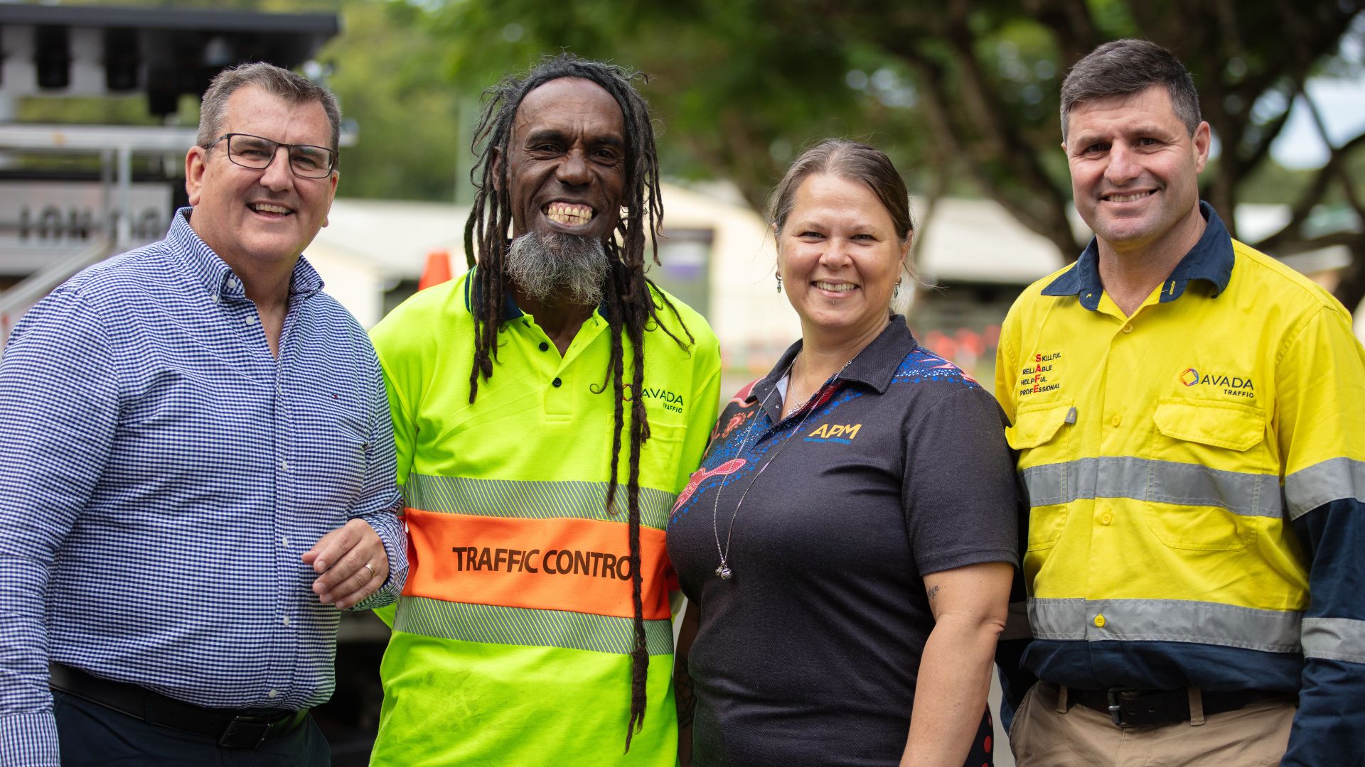 Workforce Australia participant Adam stands with his APM employment consultant Janeah in a First Nations artwork top and his employer, all smiling at the camera.