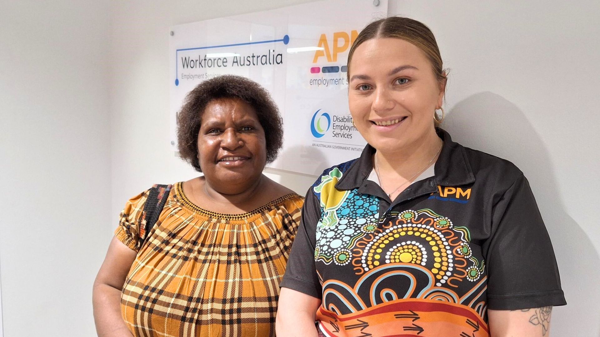 Roselyn, a Workforce Australia participant, standing with her consultant Hannah in front of an APM Employment Services sign, showcasing support for job seekers.