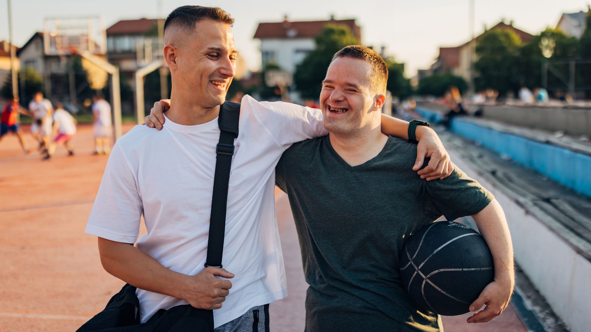 Two people smiling with their arms around each other on an outdoor basketball court.